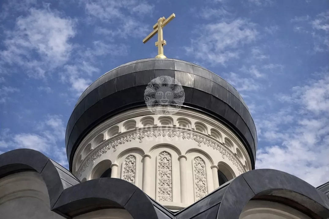 Dome with a golden cross and carved drum of the church above the rounded lines of the roof.